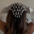 Person wearing a pearl headpiece with long, wavy hair and white gloves.